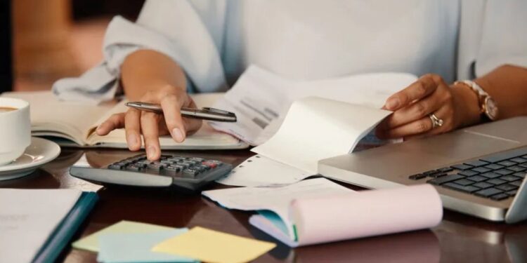 Mulher calculando dívidas e organizando boletos com calculadora e notebook para renegociação.