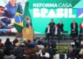 Presidente discursando no lançamento do programa Reforma Casa Brasil, com a bandeira do Brasil ao lado e painel exibindo trabalhadores da construção civil.