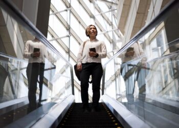 Carreiras promissoras no Brasil em 2026: salários, demanda e tendências 4 Jovem profissional em ascensão na escada rolante em prédio moderno de vidro, simbolizando o crescimento de carreira e novas oportunidades de trabalho em 2026.