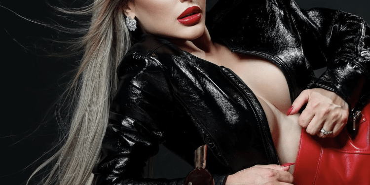 Mulher loira de batom vermelho com jaqueta preta e bolsa vermelha deitada ao lado de perfume